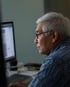 Älterer Mann mit Brille und grauem Haar schaut auf einen Computerbildschirm.