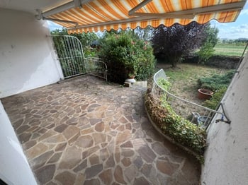 Überdachte Südterrasse mit Natursteinboden, dahinter Garten und freies Feld