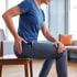 A person in a blue shirt sits on a wooden chair holding their hip and knee, appearing to be in pain.