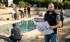 Mann mit Bauplan vor einem Pool im Bau, Arbeiter im Hintergrund.