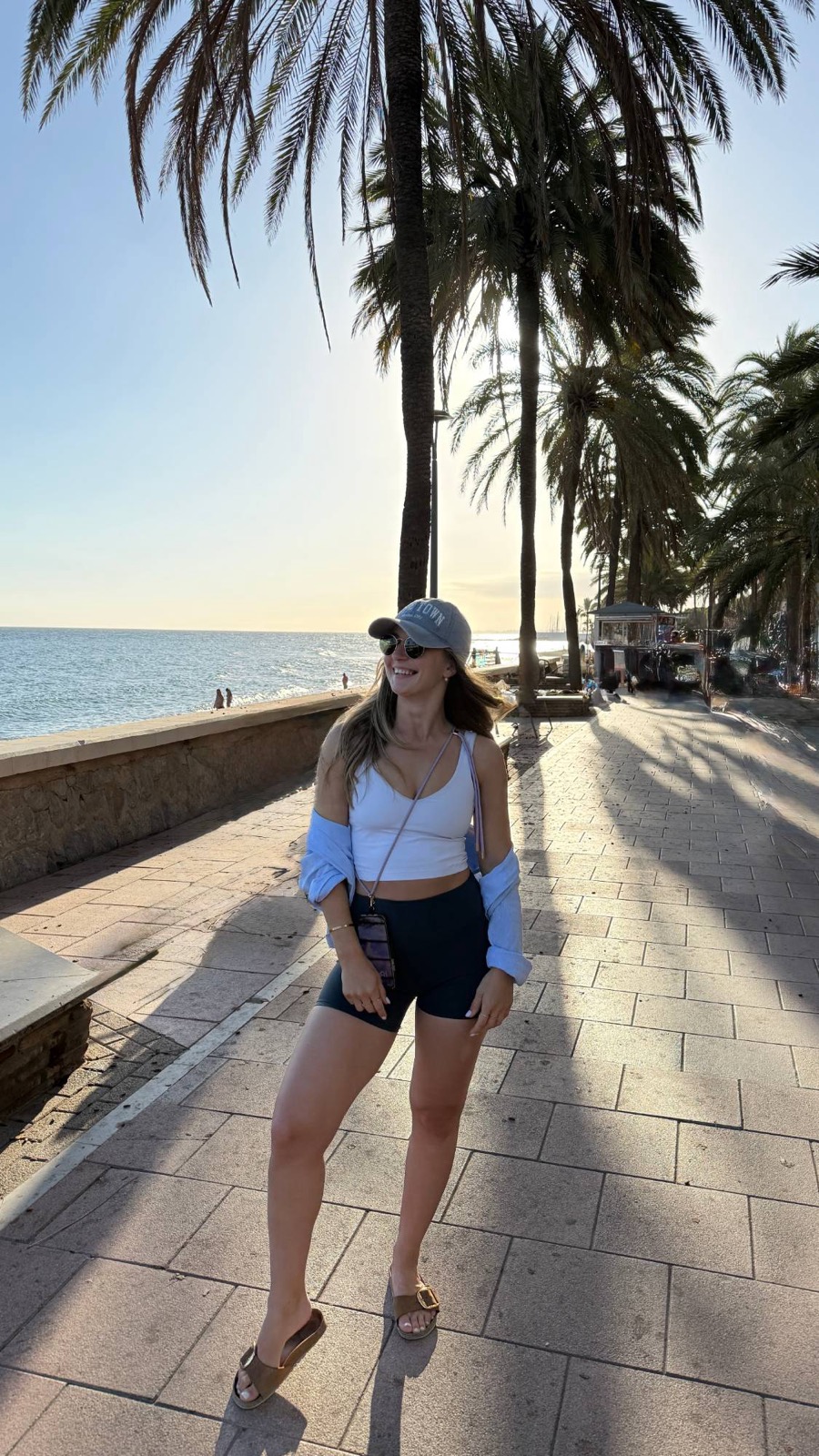 Tatjana Schäfer lacht auf einer Strandpromenade unter Palmen im Abendlicht