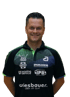 Ein lächelnder Mann in einem schwarzen Poloshirt mit Sponsorenlogos.