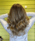 Eine Frau mit langen, gewellten blonden Haaren und einem weißen Oberteil steht vor einer gelben Wand.