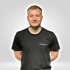 Ein lächelnder Mann mit kurzem blondem Haar trägt ein schwarzes T-Shirt mit der Aufschrift „/ SUB ZERO /“.
