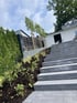 Moderne Außentreppe aus grauen Betonstufen neben einem bepflanzten Hang mit Rindenmulch und jungen Bäumen.