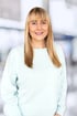 Blonde Frau mit Pony und hellblauem Pullover lächelt in die Kamera.