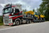 Ein weiß-roter Volvo Heavycont Lkw transportiert gelbe Wacker Neuson Baumaschinen auf einem Tieflader am Straßenrand.