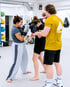 Zwei Frauen beim Boxtraining mit Handschuhen, während ein Trainer in einem gelben Shirt die Übung anleitet.