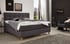 Graues Boxspringbett mit gepolstertem Kopfteil in einem Schlafzimmer mit dunkler Holzwand und Sessel.