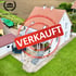 Haus mit rotem Dach und Garten, überlagert mit einem roten Stempel „VERKAUFT“; Olymp Immobilien Logo oben links