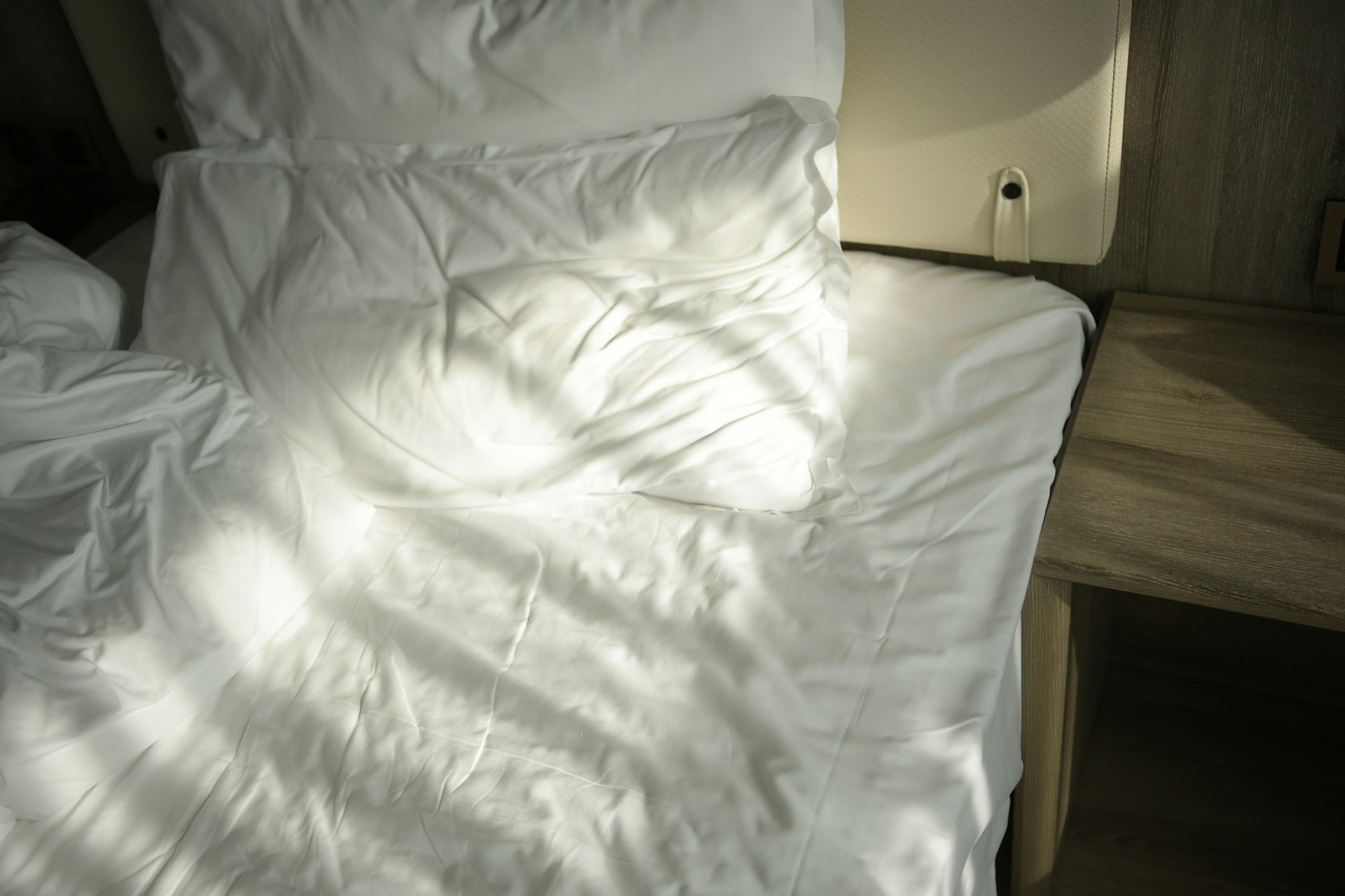 Ein zerwühltes weißes Bett mit Nachttisch im Morgenlicht