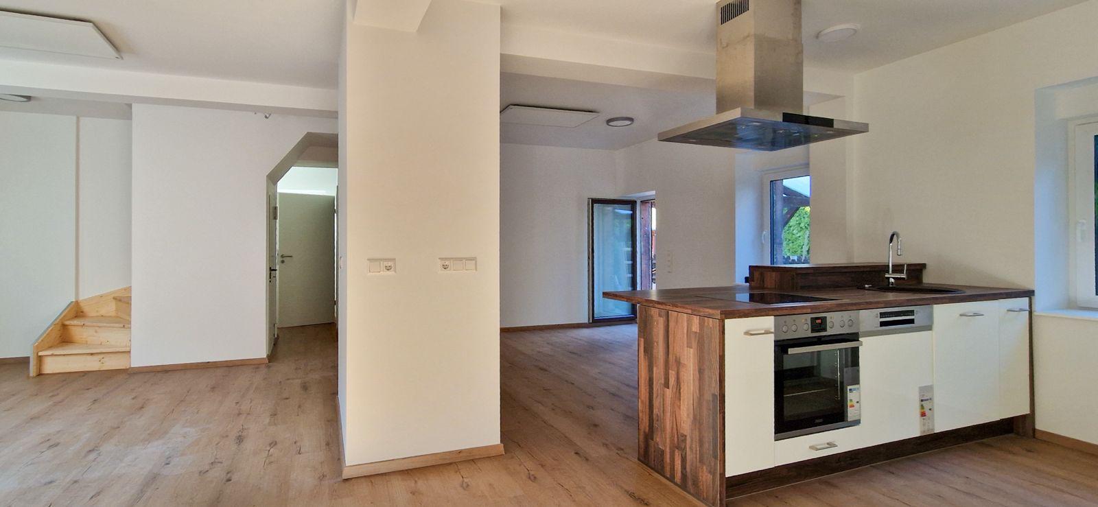 Kücheninsel mit Induktionsfeld und Backofen, dahinter der Wohnbereich und die Holztreppe