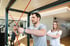 Ein Mann trainiert mit roten Widerstandsbändern an einem Trainingsgerät unter Anleitung einer Trainerin in einem Fitnessstudio.