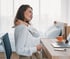 Woman in white shirt rubbing her shoulder, experiencing joint pain while sitting at a desk.