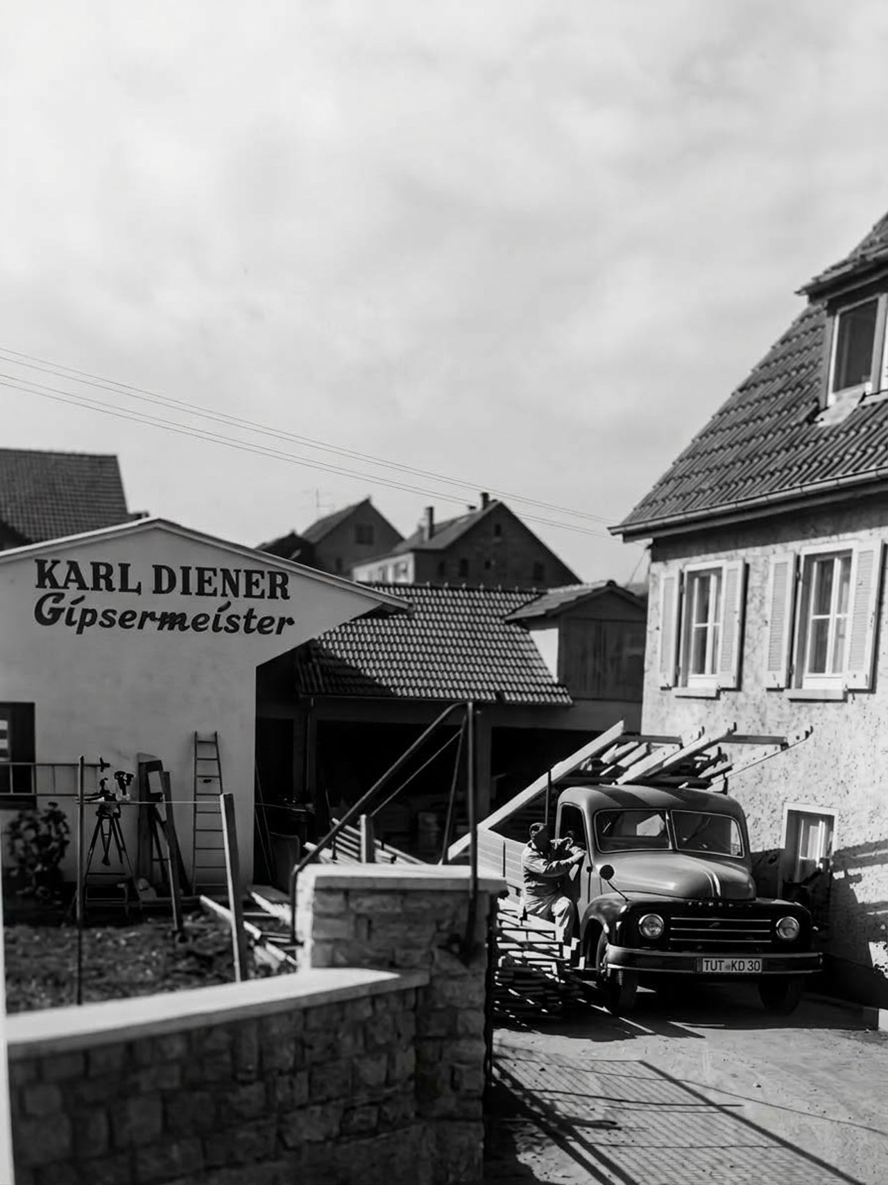 Historisches Schwarzweißfoto: Werkstattgebäude mit der Aufschrift Karl Diener Gipsermeister, davor ein Lastwagen mit dem Kennzeichen TUT-KD 30