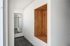 Heller Flur mit weißem Wandschrank, integrierter Holznische mit Haken und hohem Spiegel.