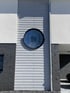 Graue Holzverkleidung und dunkelgraues Ziegelmauerwerk mit einem runden Fenster, das ein geschweiftes Klammer-Logo zeigt.