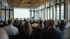 Ein Konferenzraum mit Publikum blickt auf eine Leinwand mit Text und einen stehenden Redner.