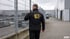 Sicherheitsmitarbeiter von LH Security Service mit Funkgerät patrouilliert an einem Zaun auf einem Betriebsgelände. KI-generiert.