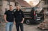 Zwei Maler stehen vor einem schwarzen SINEO-Handwerker Auto mit der Aufschrift „SINEO“, Telefonnummer und Website.