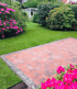Gepflasterte Terrasse aus roten Ziegeln mit Rasen und blühenden rosa Rhododendren.