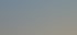 Eine Baustelle mit ausgehobener Erde, einer Schotterfläche und einem blauen Bagger unter blauem Himmel.
