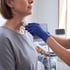 A healthcare professional in blue gloves performs a thyroid ultrasound on a patient using a handheld transducer probe.