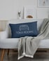 Dunkelblaues Kissen mit weißem Bettsymbol und Text "TOKA ROOMS" auf weißem Sofa mit Decke.