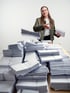 Eine Frau wirft Briefstapel auf einen großen Haufen weißer Briefumschläge auf einem Holztisch vor weißem Hintergrund.