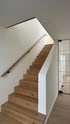 Holztreppe mit weiß gestrichenen Wänden, Holzgeländer und Glaswand mit dunklem Rahmen.