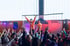 Zwei Musiker performen auf einer Bühne vor einer Menge jubelnder Kinder, ein Banner sagt "LIVE IN SCHULE".