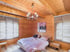 Schlafzimmer in einem Holzhaus mit Balkendecke, Kronleuchter, Doppelbett und zwei Fenstern mit Jalousien.