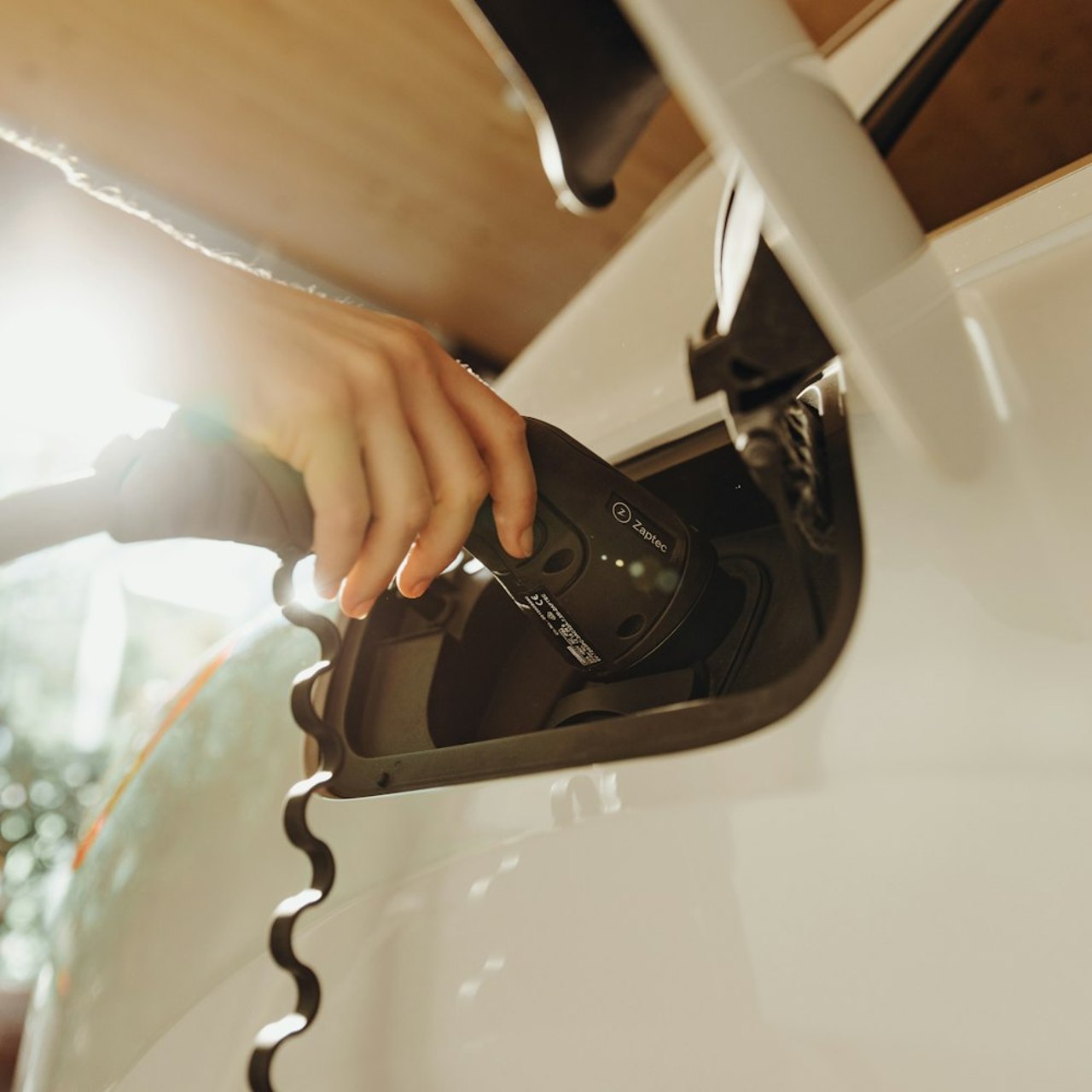 Driver plugging a charging cable into an electric car at home