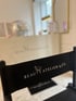 Schwarzer Klappstuhl mit weißem "BEAUTY ATELIER by Fatiha" Logo, im Hintergrund ein Schreibtisch.