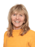 Eine lächelnde Frau mit blonden Haaren und einem orangefarbenen Pullover blickt geradeaus.