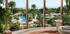 Tropical resort with multiple swimming pools, palm trees, and ocean view from a balcony.