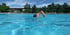 Ein Mann schwimmt Kraul im blauen Wasser eines Freibades unter blauem Himmel.