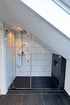 Moderne Duschkabine mit Glaswänden, weißen Fliesen, schwarzem Boden und schräger Decke.