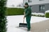 Ein Mann in grüner Winterkleidung schaufelt Schnee von einem gepflasterten Weg.