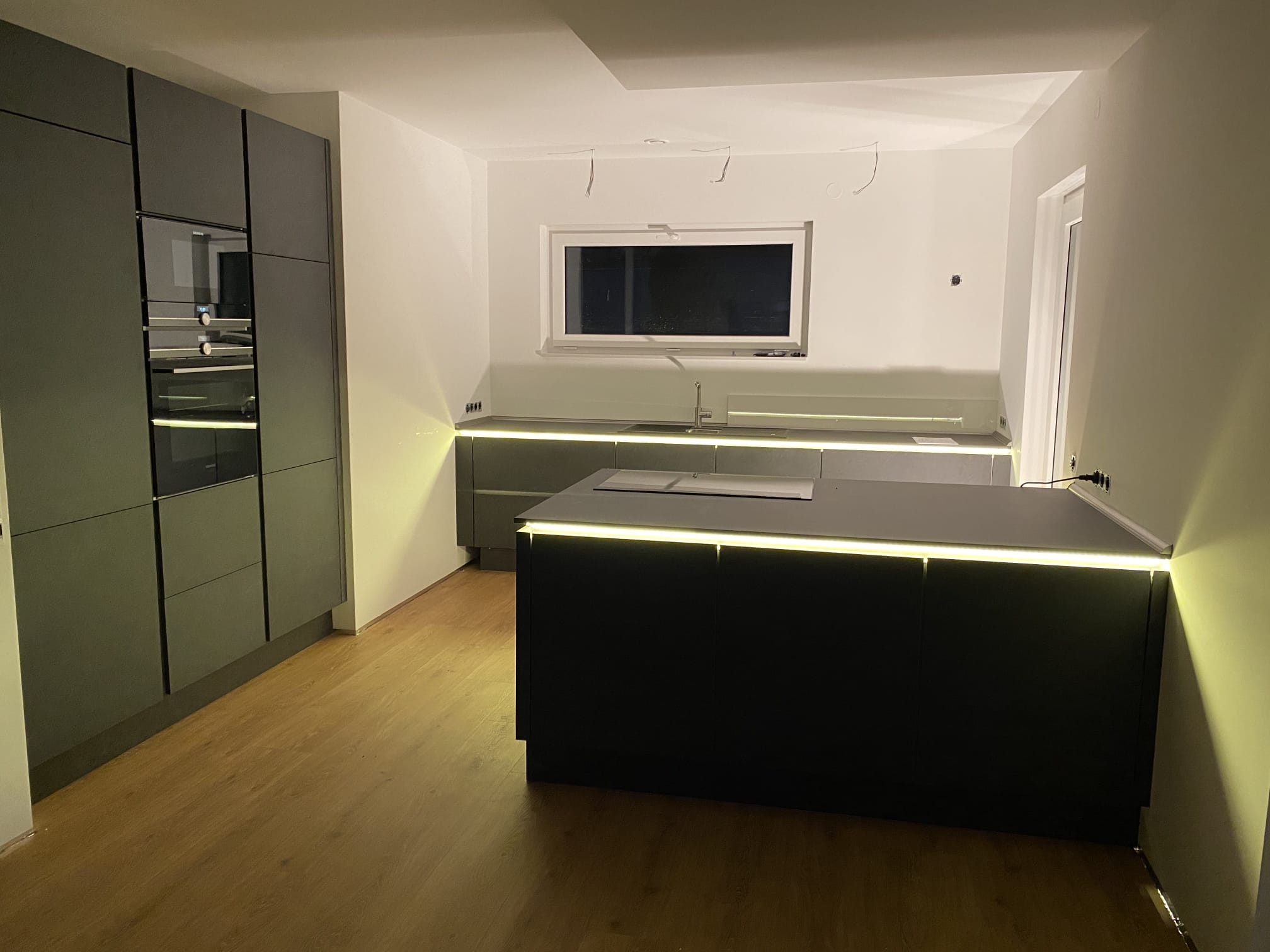 Dunkle Küche mit indirekter LED-Beleuchtung an Insel und Küchenzeile