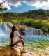 Eine Person sitzt auf einem Felsen und blickt auf einen breiten Wasserfall und einen See m Naionalpark Krka.