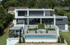 Großes, modernes Haus mit Flachdach, Pool und mehreren Terrassen, umgeben von grünen Bäumen.