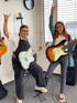 Two girls with electric guitars make rock-and-roll hand gestures.