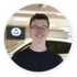 Junger Mann mit Brille lächelt vor einem Auto mit Mazda-Logo.