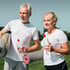 Two smiling seniors with yoga mats and water bottles stand outside on a sunny day.