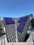 Dunkles Ziegeldach mit zwei Gruppen blauer Solarmodule unter klarem blauem Himmel.