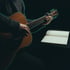 Hands on a guitar fretboard beside a notebook