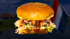 Ein Burger mit Käse, Sauce und Salat vor einer niederländischen Flagge und typischen Häusern am Wasser.