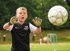 Ein junger Fußballtorwart in Handschuhen und Trikot springt, um einen weißen Fußball zu fangen.