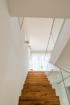 Moderne Holztreppe mit Glasgeländer und weißen Wänden in einem hellen Treppenhaus.